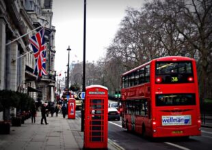 Czerwony podwójny double decker autobus na ulicy Londynu obok budki telefonicznej i flaga Wielkiej Brytanii