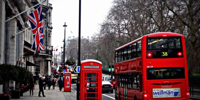 Czerwony podwójny double decker autobus na ulicy Londynu obok budki telefonicznej i flaga Wielkiej Brytanii