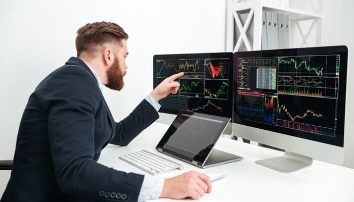 Mężczyzna analizujący wykresy na dwóch monitorach