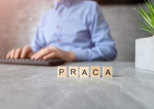 Klocki z napisem praca na biurku, w tle osoba przy klawiaturze