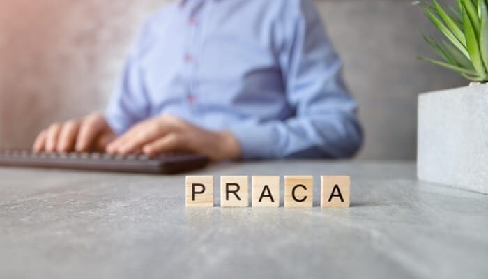 Klocki z napisem praca na biurku, w tle osoba przy klawiaturze