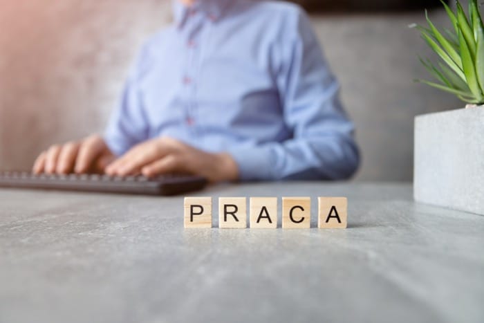 Klocki z napisem PRACA na biurku, w tle osoba przy klawiaturze